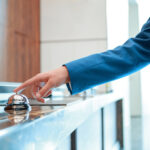 Service, please. Closeup of a businessman hand ringing silver service bell on hotel reception desk