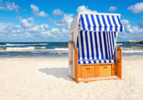 Blue and white wicker chair on sandy beach with cloud