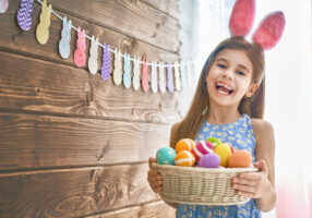 Cute little child wearing bunny ears on Easter day. Girl holding basket with painted eggs.