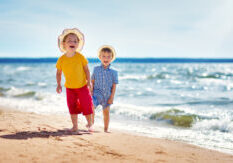 Boy and girl playing on the beach on summer holidays. Children in nature with beautiful sea, sand and blue sky. Happy kids on vacations at seaside running in the water